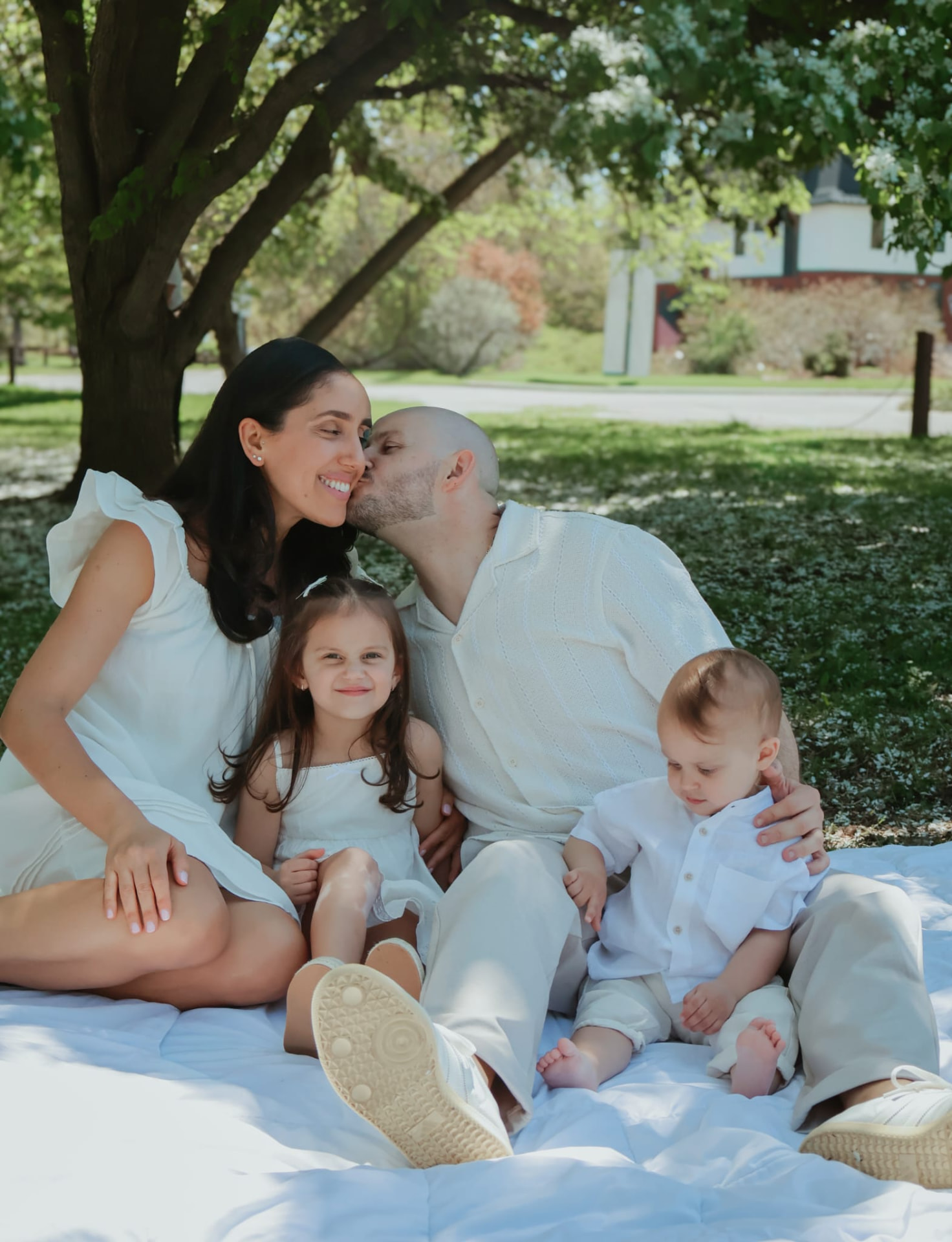 Family of four sitting together on a white blanket under a blossoming tree